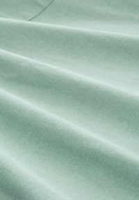 Țesătură de bumbac verde mentă cu o textură netedă, având pliuri delicate și un luciu subtire, evidențiind calitatea sa ușoară și respirabilă.