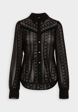 Blouse noire à manches longues en dentelle avec motif floral, boutonnée sur le devant, col pointu et taille cintrée.