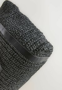 Panier tissé noir avec une surface texturée, arborant une bande d'accent en cuir noir lisse et des coutures blanches le long du bord supérieur.