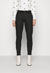 Czarne wąskie spodnie o gładkiej fakturze, z zapięciem na guziki z przodu i szlufkami na pasek, w zestawieniu z białym swetrem w groszki oraz jasnymi botkami za kostkę.