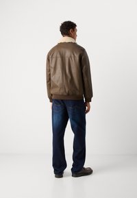 Giacca di pelle marrone con colletto in pelliccia sintetica, abbinata a jeans blu scuro a vestibilità ampia e scarpe nere, vista da dietro.