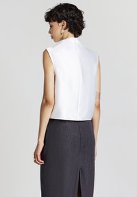 Top bianco senza maniche con collo alto e texture liscia, abbinato a una gonna grigio scuro con uno spacco frontale e un sottile motivo verticale.