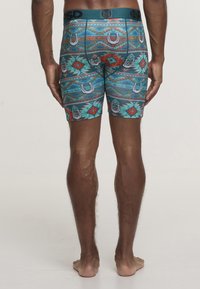 Kolorowe bokserki w stylu trunk z geometrycznym wzorem z podkową, w odcieniach turkusu, czerwieni i zieleni; wykonane z miękkiej, elastycznej tkaniny.