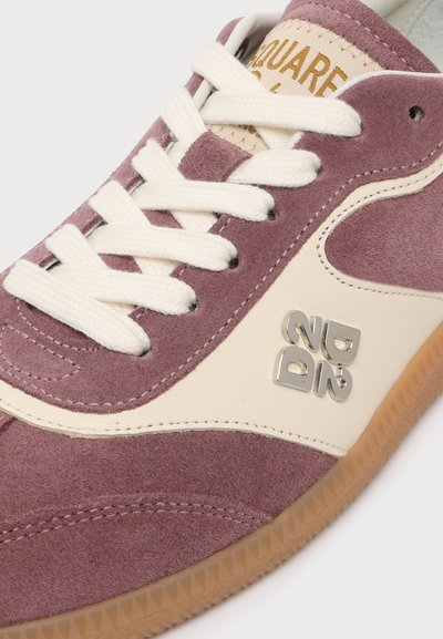 Gros plan sur une basket en daim violet avec des lacets blancs, un panneau latéral crème, une semelle en gomme et un logo métallique "D22" sur le côté.