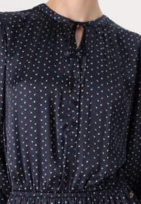 Laivastonsininen paita, jossa on punaisia ja valkoisia pilkkuja, napitettava etukappale, kerätty pääntie siteellä ja joustava vyötärö.