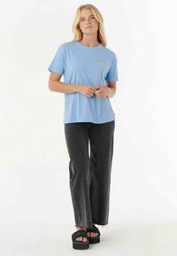 Jasnoniebieski bawełniany t-shirt z krótkimi rękawami i małym logo na piersi, zestawiony z wysokim stanem ciemnoszarych rozkloszowanych dżinsów i czarnymi sandałami na platformie.