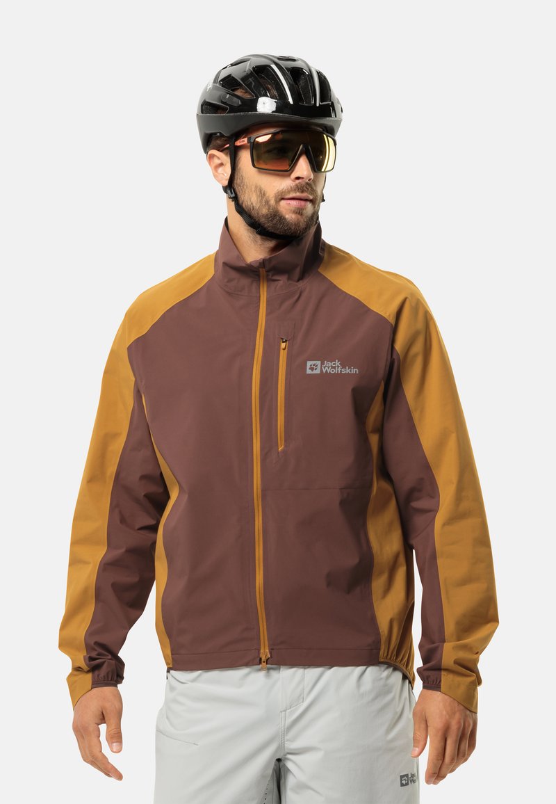 Bordauxrode en amberkleurige waterdichte jas met een hoge kraag, een ritszak aan de voorkant en elastische manchetten. Draagt een zwarte helm en een zonnebril.