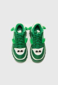 Sneakers verdi con una morbida texture in suede, ampie rifiniture bianche con occhi neri e elementi decorativi verdi sui lati.