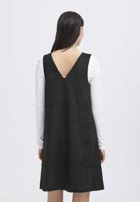 Schwarzes, ärmelloses Kleid mit tiefem V-Ausschnitt im Rücken, aus weichem, samtartigem Material gefertigt, mit einer lockeren, A-Linien-Form und ohne sichtbare Verschlüsse.