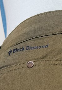 Olivově zelená tkanina s našitým lemem, logo "Black Diamond" v námořnické modři a kovový knoflík se jménem značky.
