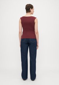 Top senza maniche color bordeaux abbinato a jeans a gamba larga blu scuro. Il top presenta un leggero scollo a barca; i jeans hanno tasche standard e cuciture.