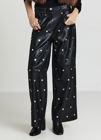 Schwarze Lederhose mit weitem Bein und silbernen runden Nieten, ausgestattet mit Seitentaschen und hohem Bund. Kombiniert mit schwarzen Stiefeletten mit Absatz.