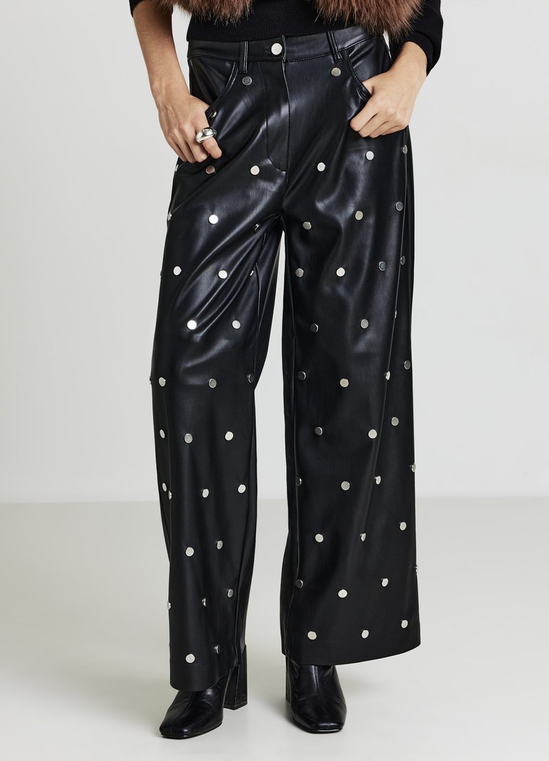 Schwarze Lederhose mit weitem Bein und silbernen runden Nieten, ausgestattet mit Seitentaschen und hohem Bund. Kombiniert mit schwarzen Stiefeletten mit Absatz.
