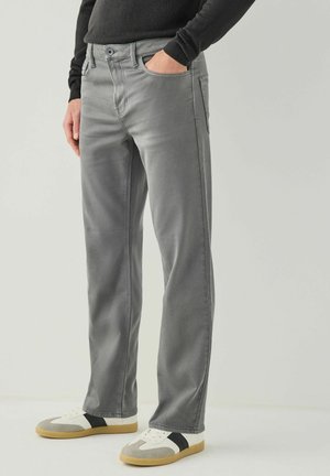 Graue Baumwolldenim-Hosen mit geradem Schnitt, Fünf-Taschen-Design und Kontrastnähten, kombiniert mit leichten Sneakers in Beige und Schwarz.