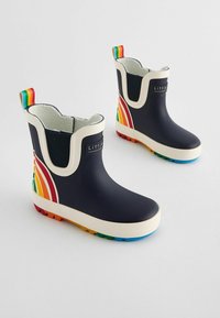 Bottes de pluie en caoutchouc bleu marine avec des accents blancs, présentant un design de rayures arc-en-ciel sur les côtés et des semelles multicolores. Forme courte et arrondie.