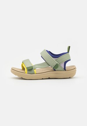 Green fabric sandals with adjustable straps, featuring yellow and purple accents, a cushioned beige sole, and a textured footbed.