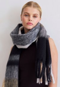 Écharpe en laine gris et noir offrant une texture douce, un design ample et des bords fringés. Motif dégradé subtil allant du clair au foncé.