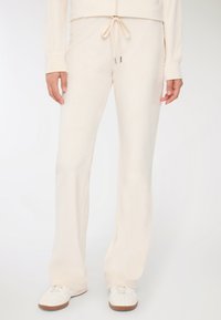 Kremowe spodnie o luźnym kroju, wykonane z miękkiego materiału, z elastyczną talią i rozszerzanymi nogawkami. W połączeniu z białymi trampkami.