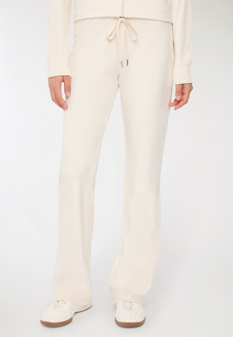 Kremowe spodnie o luźnym kroju, wykonane z miękkiego materiału, z elastyczną talią i rozszerzanymi nogawkami. W połączeniu z białymi trampkami.