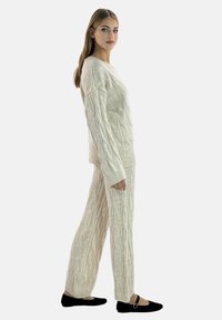 Sæt med cremefarvet kabelstrikket sweater og bukser med lange ærmer, brede manchetter og afslappet pasform. Sorte flade sko fuldender outfittet.