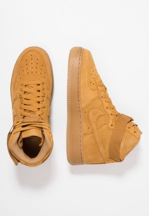 Paire de baskets montantes en daim beige avec bout perforé, semelle épaisse, fermeture à lacets à l’avant et bride de cheville ajustable sur fond blanc.
