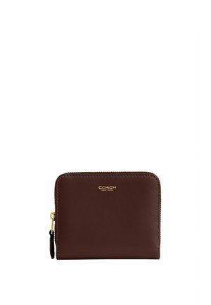 Portefeuille en cuir marron avec fermeture éclair autour, logo Coach New York doré et tirette de fermeture dorée sur fond blanc.