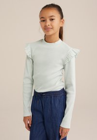 Svijetlozelena majica s dugim rukavima, rebraste teksture, s naboranim detaljima na ramenima, u kombinaciji s tamnoplavim hlačama s elastičnom pasicom.
