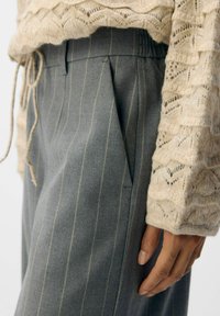 Grau gestreifte Hose mit einem strukturierten beigen Pullover. Die Hose hat einen bequemen elastischen Bund und seitliche Taschen.