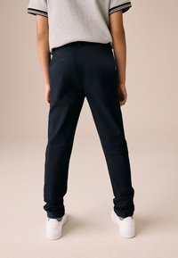 Tengerészkék nadrág szabott fazonban, sima anyagból készült, egyetlen hátsó zsebbel, fehér tornacipővel párosítva.