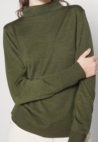 Olive green pullover sweater with a high neckline, ribbed texture, and fitted cuffs. Fabric appears soft and lightweight.