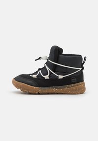 Zapatilla negra tipo media, con parte superior de tejido texturizado, sistema de cordones blanco y suela de goma marrón moteada.