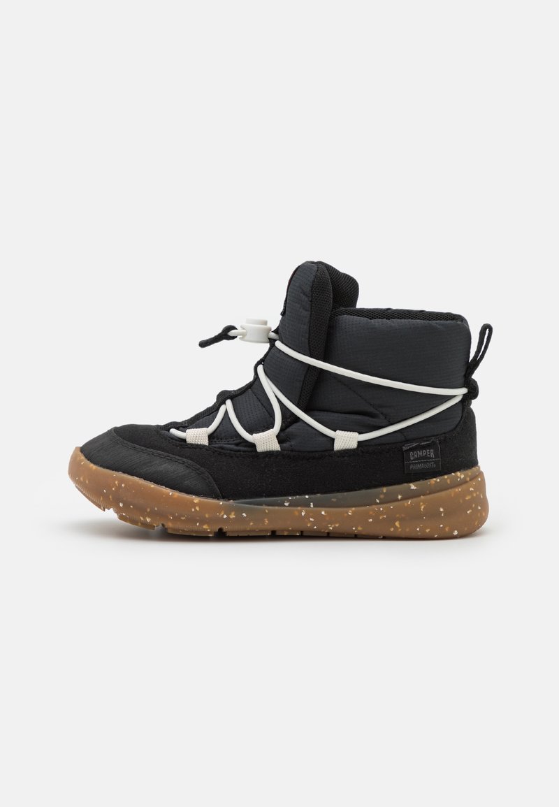 Zapatilla negra tipo media, con parte superior de tejido texturizado, sistema de cordones blanco y suela de goma marrón moteada.