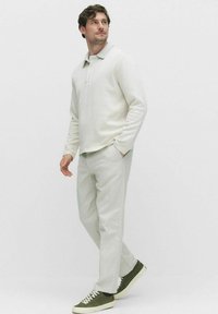 Krämfärgad långärmad polo, avslappnad passform. Kombinerad med ljusfärgade byxor och gröna sneakers. Slät textil, minimalistisk design.