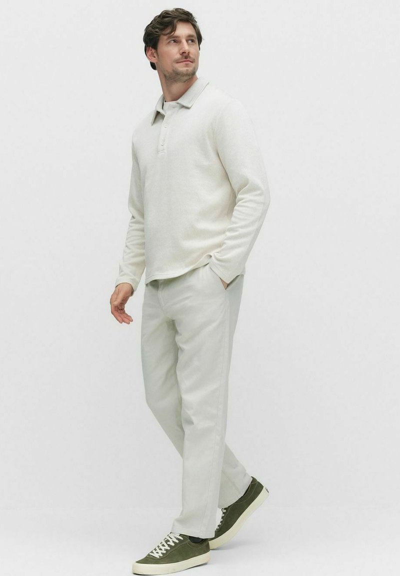 Krämfärgad långärmad polo, avslappnad passform. Kombinerad med ljusfärgade byxor och gröna sneakers. Slät textil, minimalistisk design.