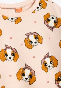 Roze sweatshirt met een zachte textuur, voorzien van een herhalend patroon van cartoon hondengezichten met haarbanden en kleine harten als accenten.