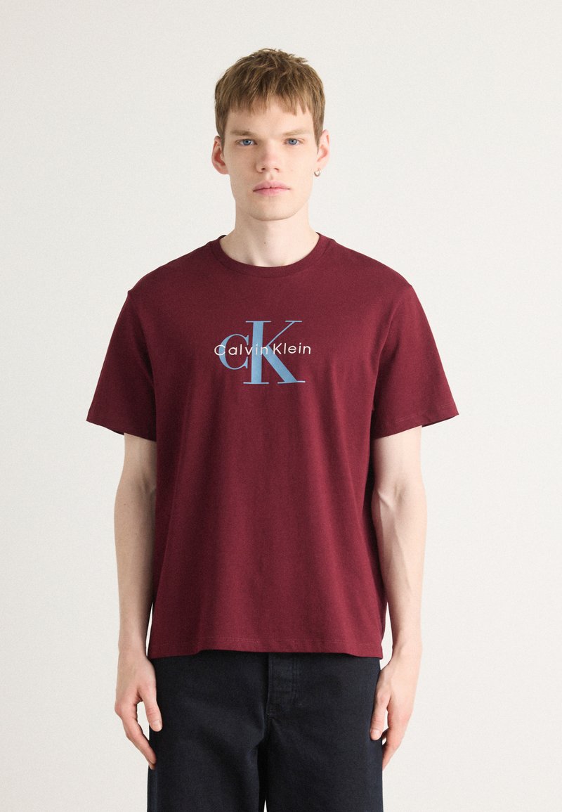 Bordo pamučna majica s okruglim izrezom i kratkim rukavima, s plavim i bijelim logotipom koji glasi "Calvin Klein."