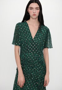 Groene jurk met luipaardprint, diepe V-hals en doorschijnende, speelse mouwen. Heeft geplooide lagen en metalen accenten door de hele stof.