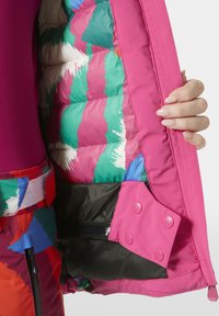 Barevná zateplená bunda s růžovým vnějškem, vícebarevným interiérem s prošívanými vzory a černými akcenty uvnitř.
