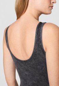Body negru, fără mâneci, cu spate decupat. Material neted, texturat, cu un model marbrat subtil, având bretele late și o formă ajustată.