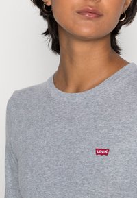 Harmaa puuvillainen pitkähihaisessa paidassa on pyöreä pääntie ja vasemmassa rinnassa pieni punainen Levi's-logopatch.