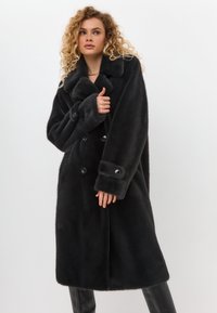 Schwarzer Kunstfellmantel mit doppelter Knopfleiste, großem Kragen und geknöpften Ärmelbündchen. Weiche Textur mit schlanker Silhouette.