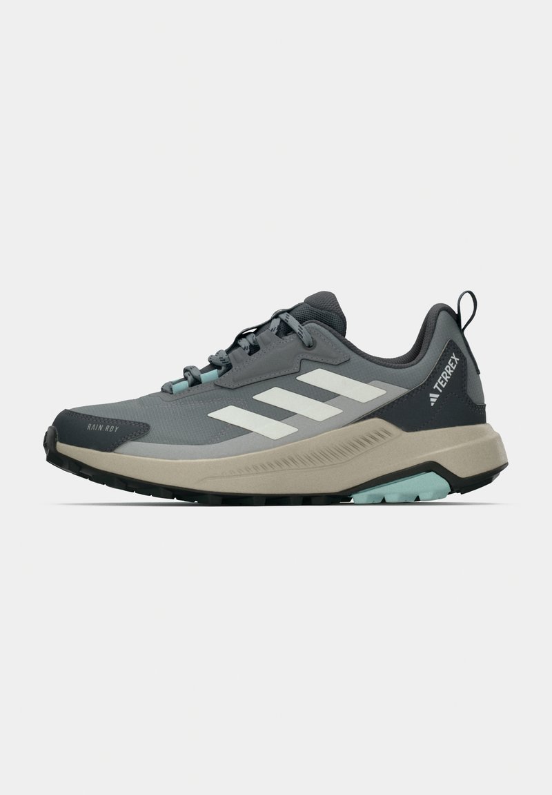 Сиви и черни туристически обувки Adidas Terrex с бели ивици и бежова подметка, страничен изглед на бял фон.