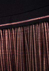 Faltenrock aus strukturiertem, metallic-bronzefarbenem Stoff, mit einem einfarbigen schwarzen Bund, der von einem dünnen, glitzernden roségoldenen Streifen akzentuiert wird.