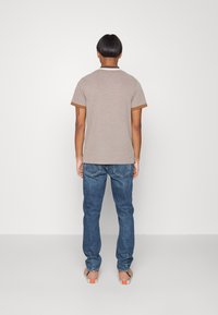 Camisa marrón de manga corta con cuello en contraste, combinada con jeans de mezclilla azules. La textura parece suave y casual, adecuada para el uso diario.