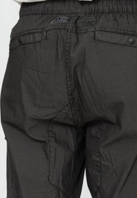 Pantaloni cargo grigio scuro con vestibilità ampia, vita elastica e tasche a patta con bottoni a pressione. Tessuto strutturato con cuciture visibili.