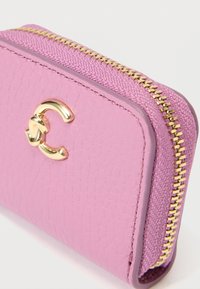 Ροζ δερμάτινο πορτοφόλι με υφή, που διαθέτει χρυσό φερμουάρ και έναν έντονο χρυσό λογότυπο στο μπροστινό μέρος.