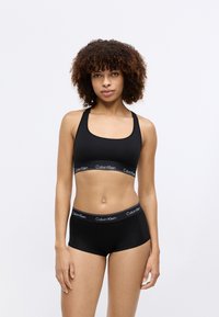 Fekete pamut sportmelltartó és boxeralsó széles elastikus pánttal, amelyen a "Calvin Klein" logó fehér színben szerepel. Sima textúra, szoros illeszkedés.