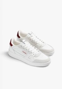 White sneakers featuring a mixed material design with leather and suede accents, red branding, and a textured sole.