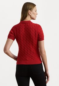 Pull en maille rouge à manches courtes, avec un col et un ourlet côtes, présentant un motif texturé pour un intérêt visuel.
