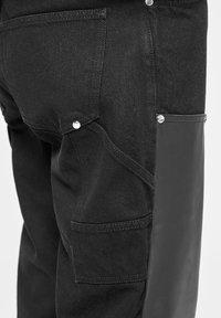 Schwarze Denim-Cargo-Hosen mit einem Leder-Seitenpaneel, sichtbaren Nähten und silbernen Nieten-Details an den Taschen.